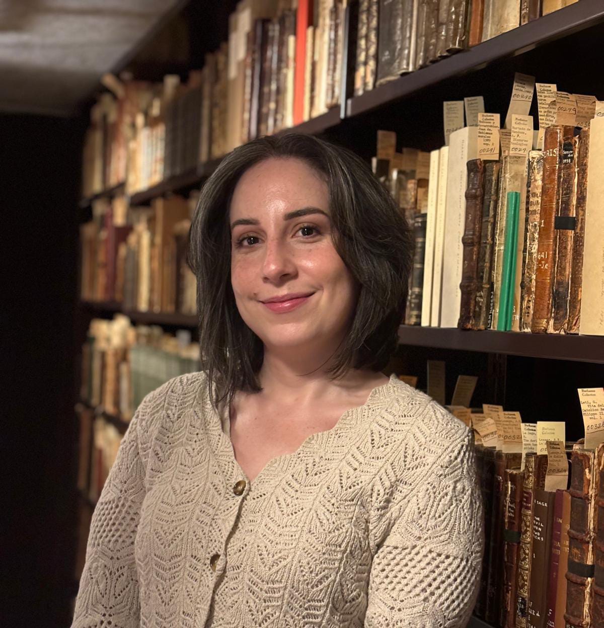 Person smiling in a library with shelves of old books.